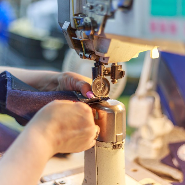 Close up of two hands holding a piece of fabric under the needle of a sewing machine with a bright light shinning.